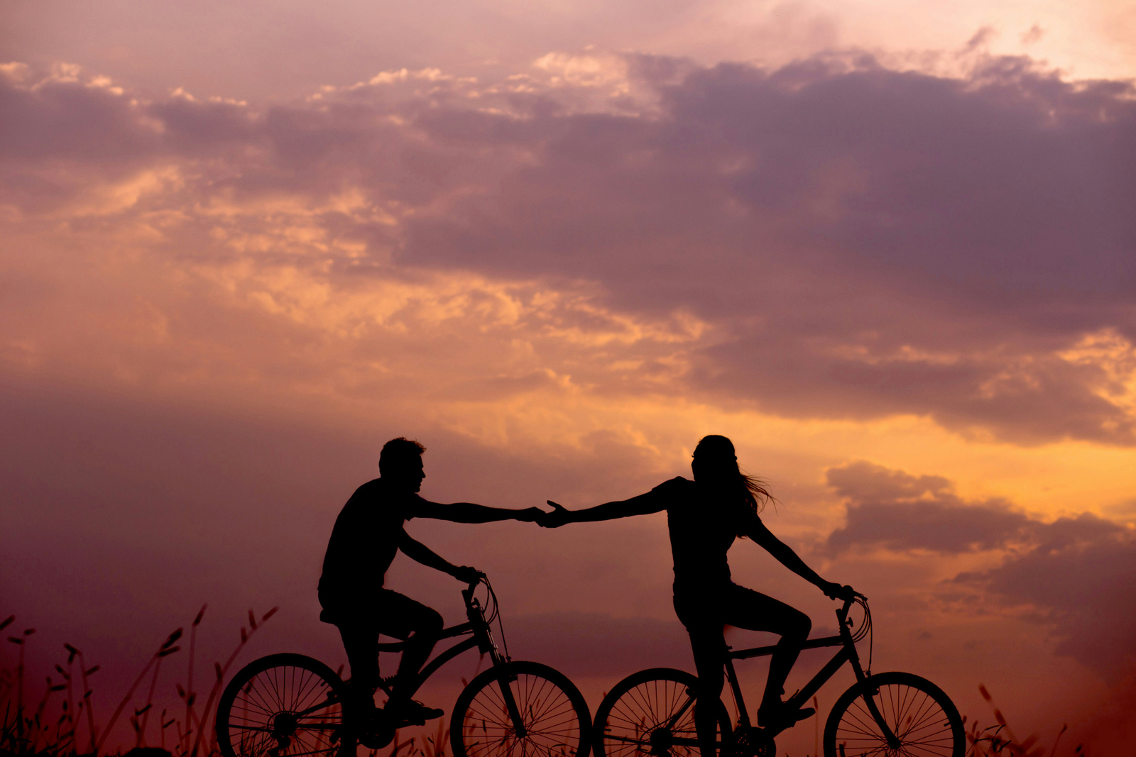 Twee fietsers houden elkaars hand vast tijdens het fietsen bij zonsondergang.