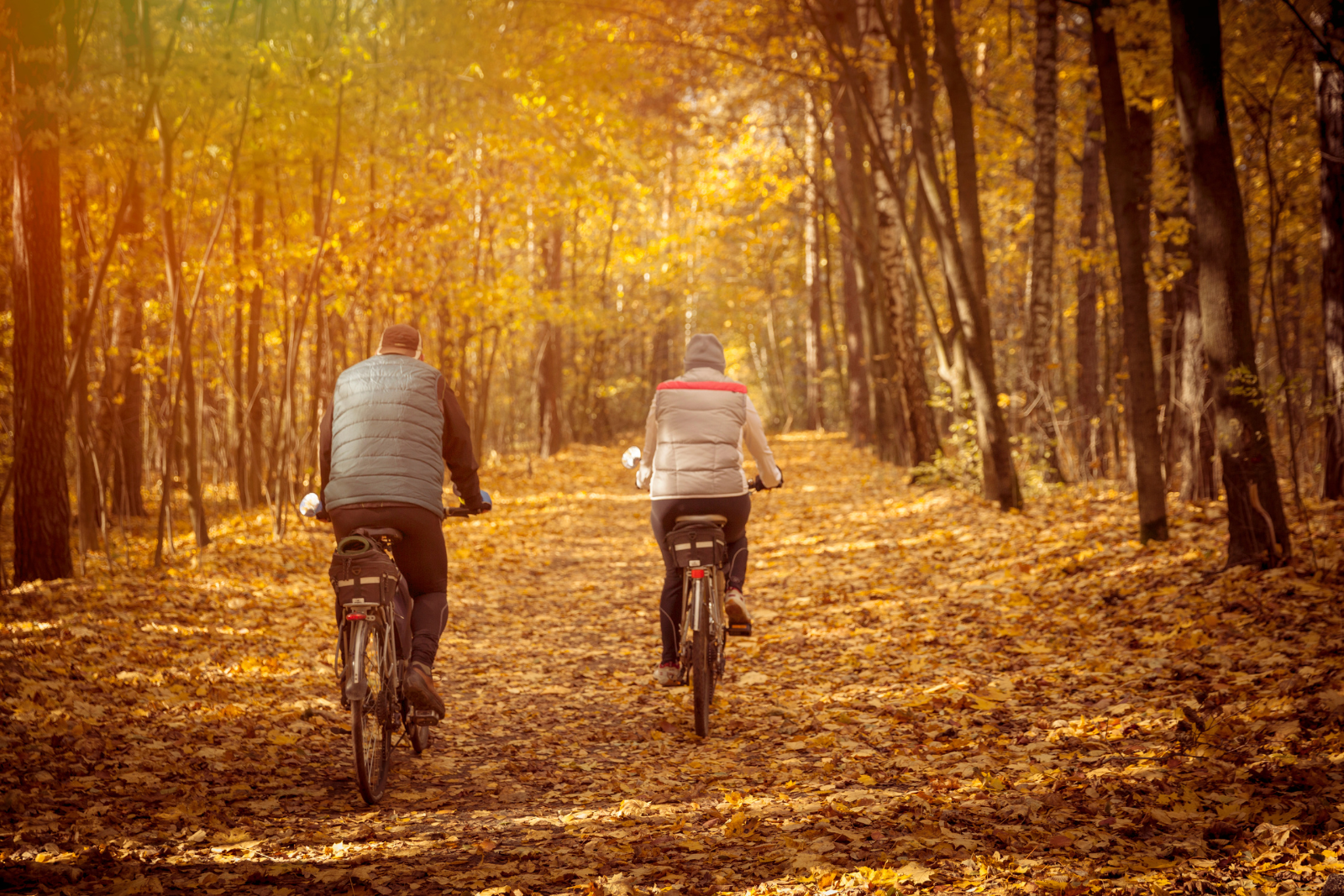 Twee fietsers rijden door een herfstbos en dragen meerdere kledinglagen tegen de kou.