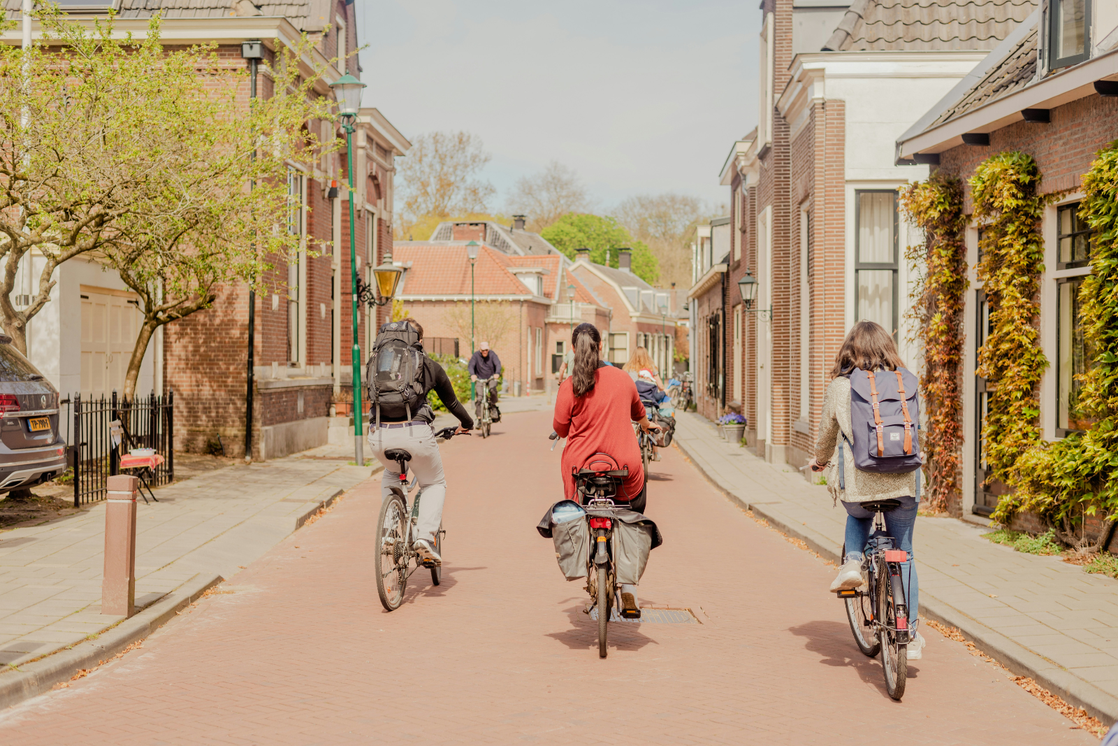 Drie mensen fietsen door een rustige straat met huizen aan weerszijden.