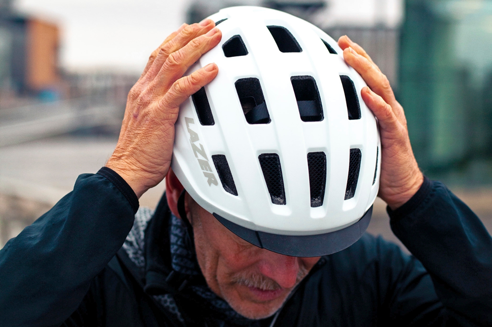 Man zet een witte fietshelm op en controleert of deze goed op zijn hoofd zit.