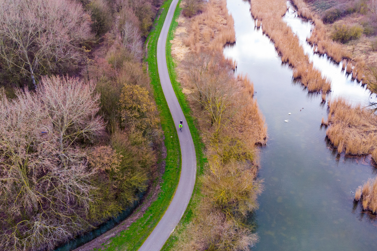 Luchtfoto van twee fietsers op een pad door de Carnisse Grienden, langs water, riet en bomen.