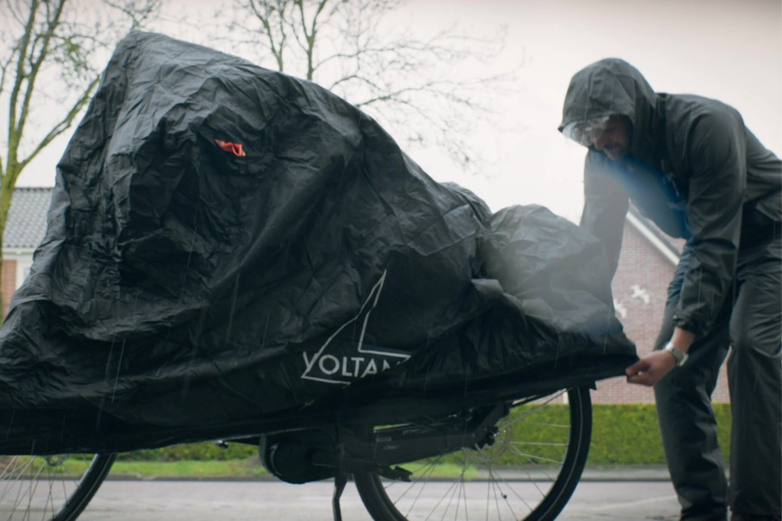 Iemand trekt een beschermhoes over een fiets om deze te beschermen tegen regen en vuil.