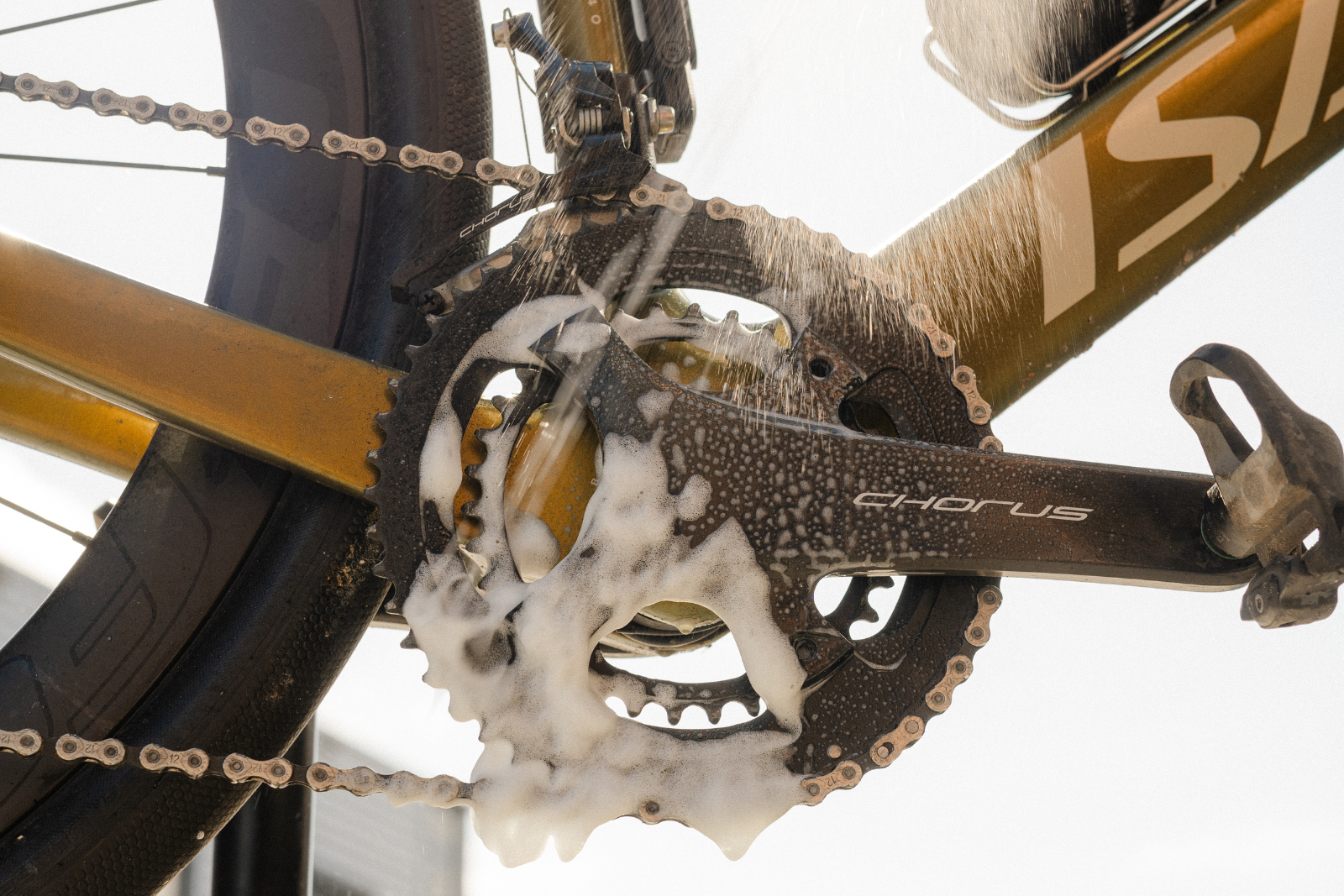 Close-up van de ketting en tandwielen van een fiets die met water en sop worden schoongemaakt.