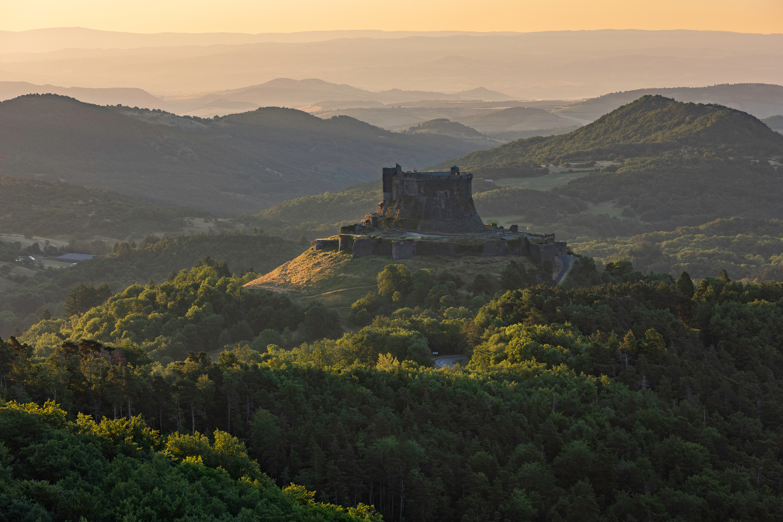Kasteel van Murol tussen de groene heuvels van de Auvergne in het avondlicht.