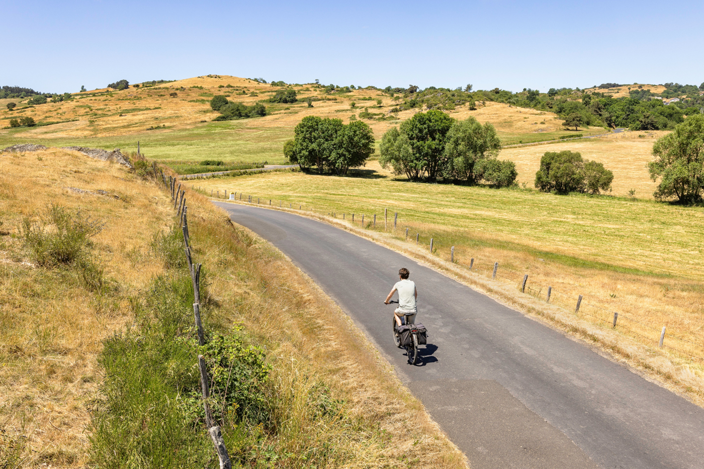 Fietser op een stille weg door het glooiende, landelijke landschap van de Auvergne.
