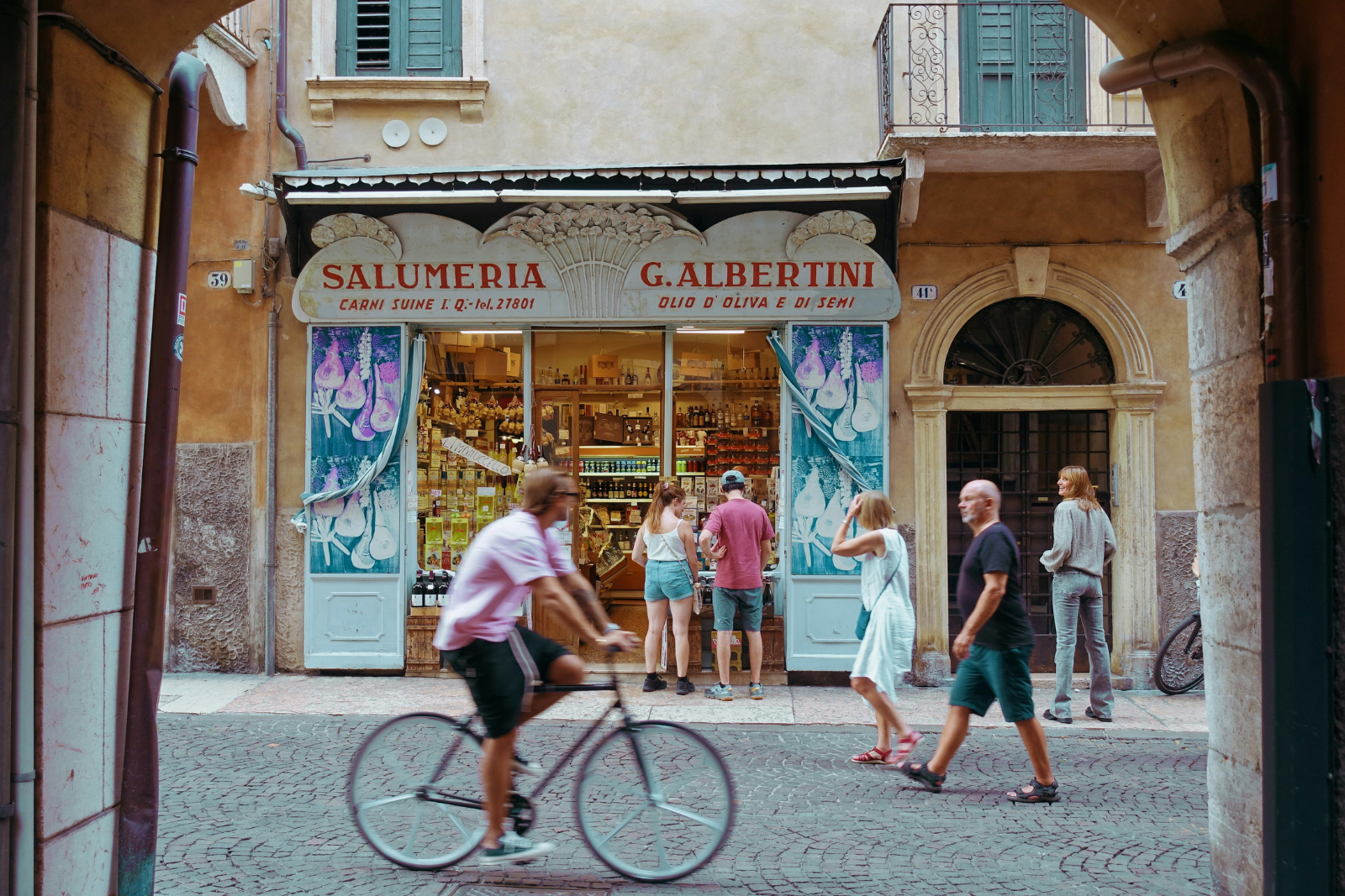 Man fietst door een sfeervolle straat in Verona, langs een traditionele Italiaanse delicatessenwinkel.