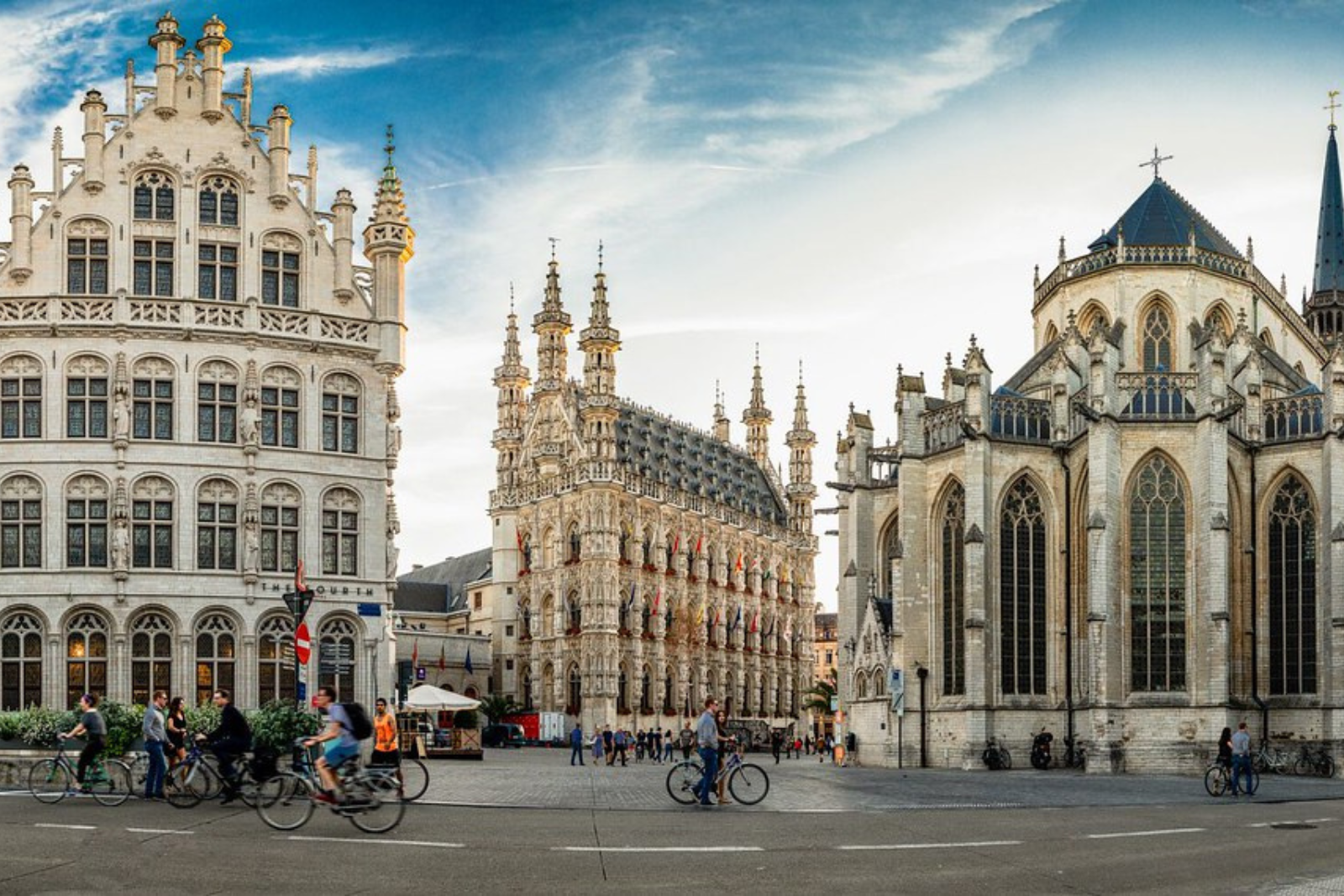 Fietsers op de Grote Markt in Leuven, met het historische stadhuis en de Sint-Pieterskerk op de achtergrond.