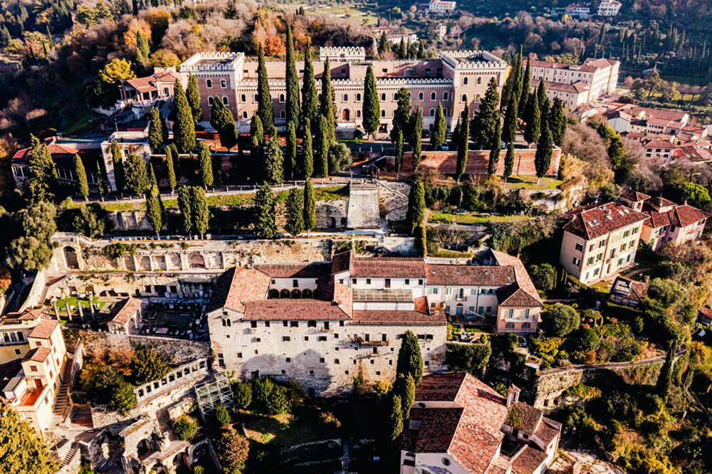 Uitzicht op Castel San Pietro op de heuvel boven Verona, omringd door cipressen en historische gebouwen.