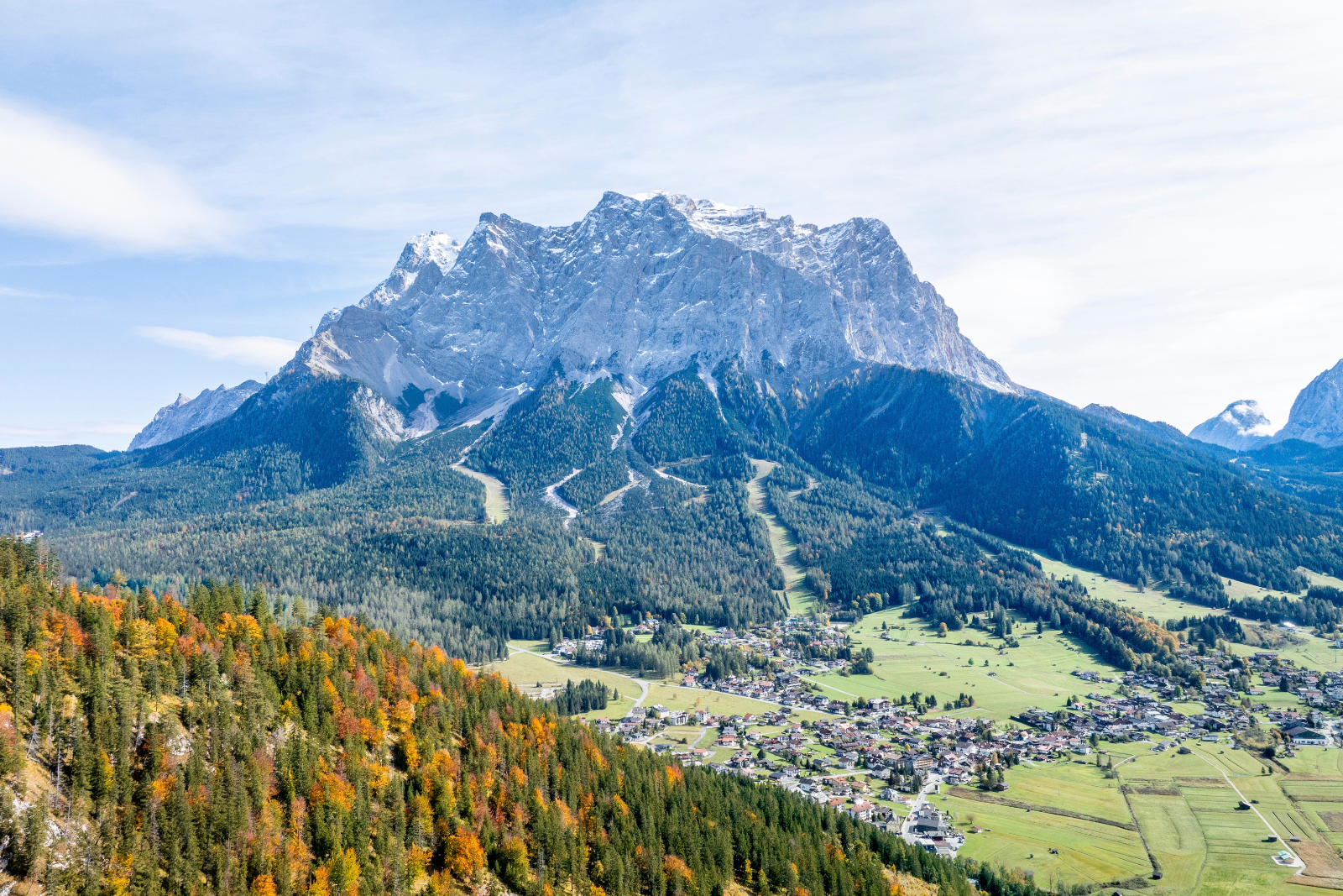 Uitzicht over het dal van de Tiroler Zugspitz Arena met groene weiden, dorpen en hoge bergtoppen op de achtergrond.