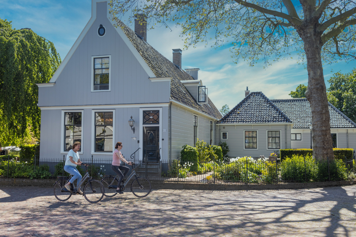 Twee fietsers rijden door Broek in Waterland langs karakteristieke houten huizen.