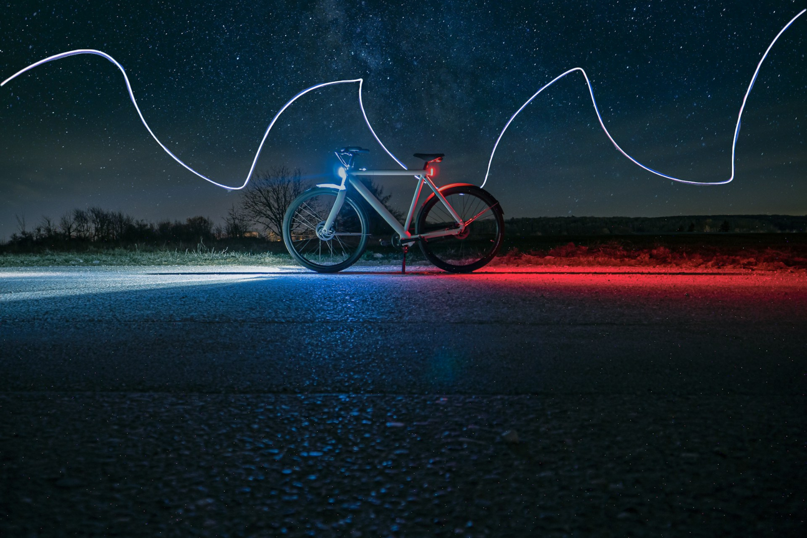 Fiets met brandend voorlicht en rood achterlicht op een donkere weg onder een sterrenhemel.