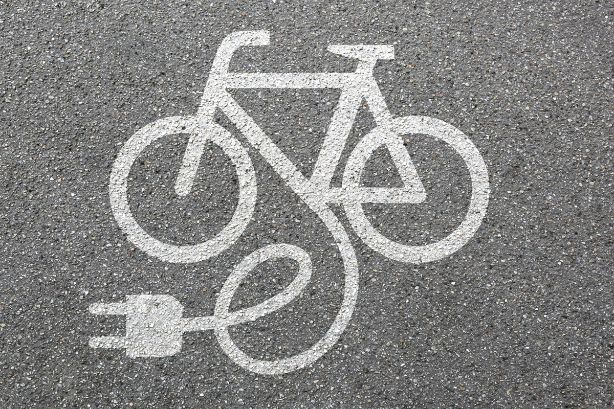 Wit symbool van een fiets met stekker op het wegdek, als aanduiding voor het opladen van een e-bike.