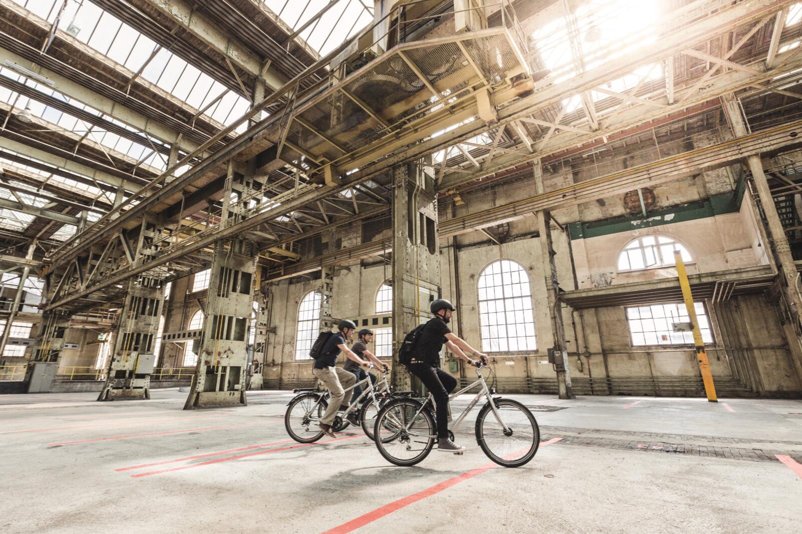 Drie fietsers rijden door een voormalige fabriekshal in Winterthur, omringd door staalconstructies en grote ramen.